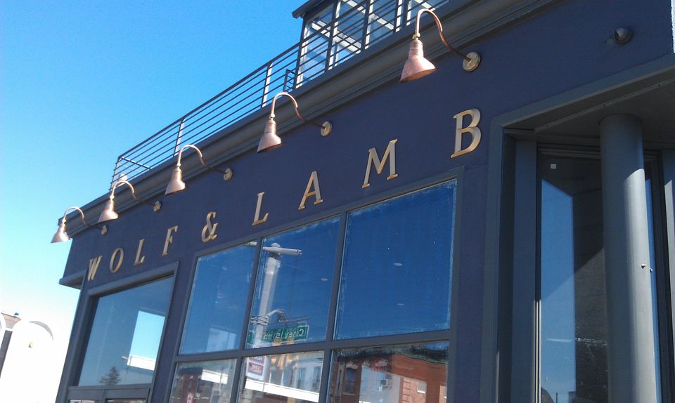Gold pin-mounted serif letters spanning a dark navy storefront facade beneath copper gooseneck lights