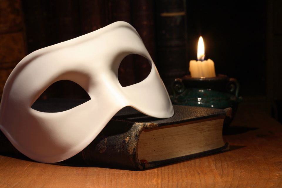 A white opera mask on a book with a candle lit in the back