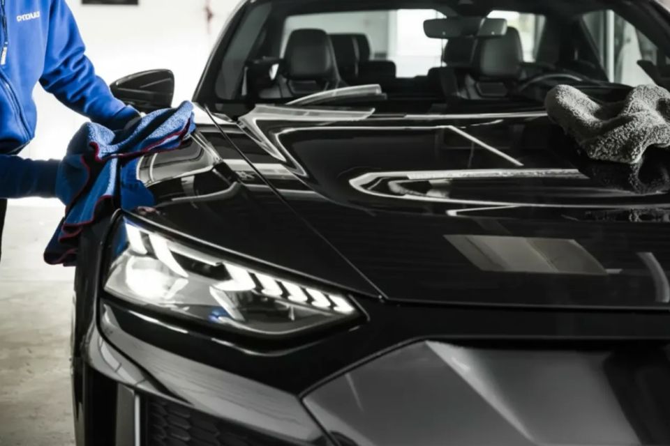 Professional auto detailer applying ceramic coating and paint correction to a black vehicle hood.