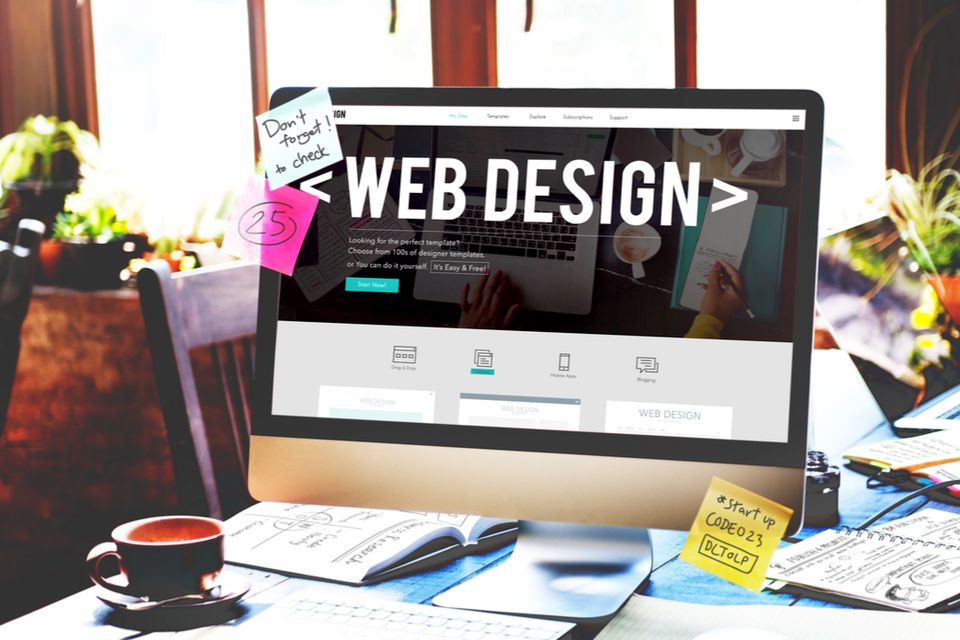 A computer screen displaying a webpage with the title "WEB DESIGN" surrounded by a workspace featuring coffee, sticky notes, a notebook, and a pen, emphasizing creativity and organization.