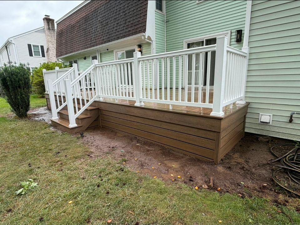 Composite deck with white vinyl railings and stairs behind green home in Virginia Beach VA
