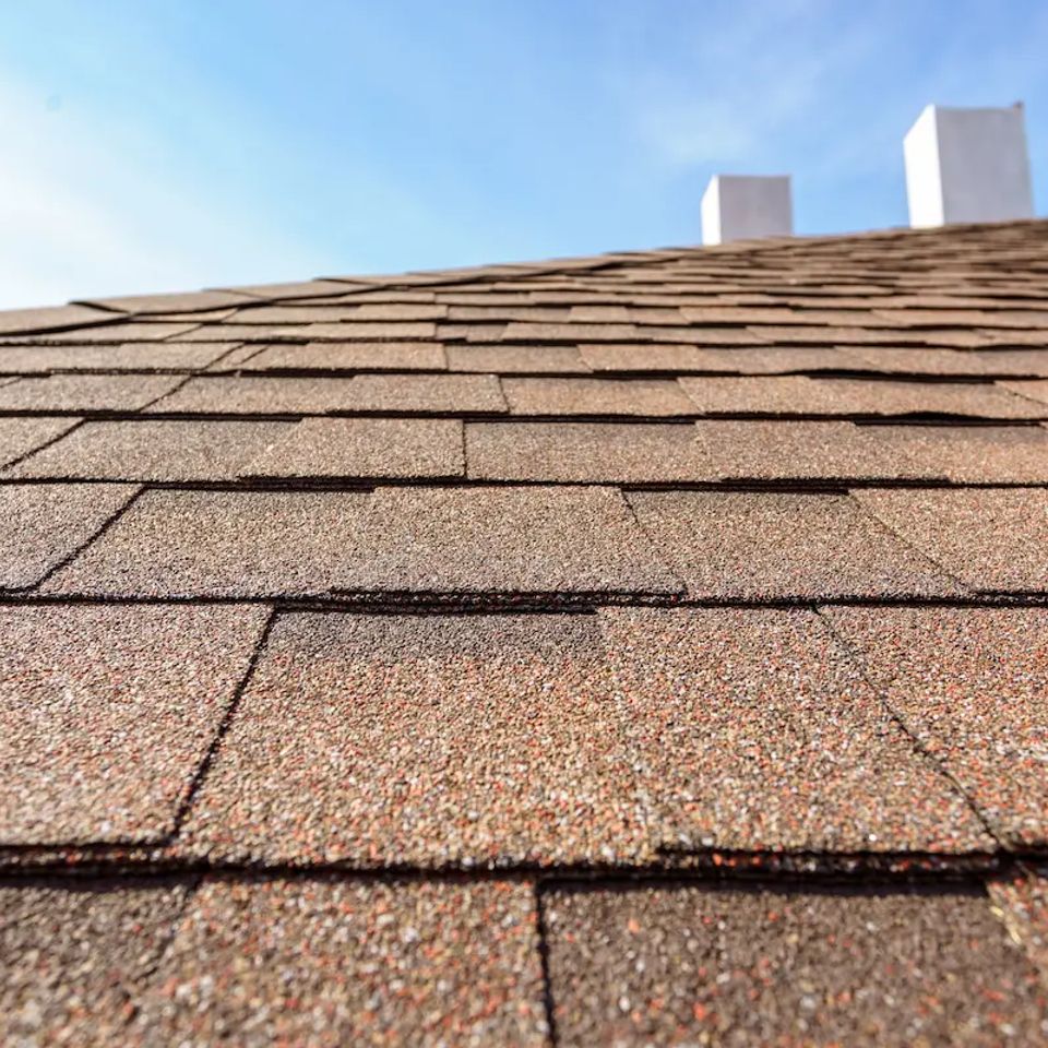 Close up photo layer of new asphalt shingles on roof top of new house under construction with chimney and blue sky 