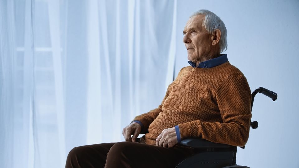 Dreamy senior man in wheelchair sitting at retirement home