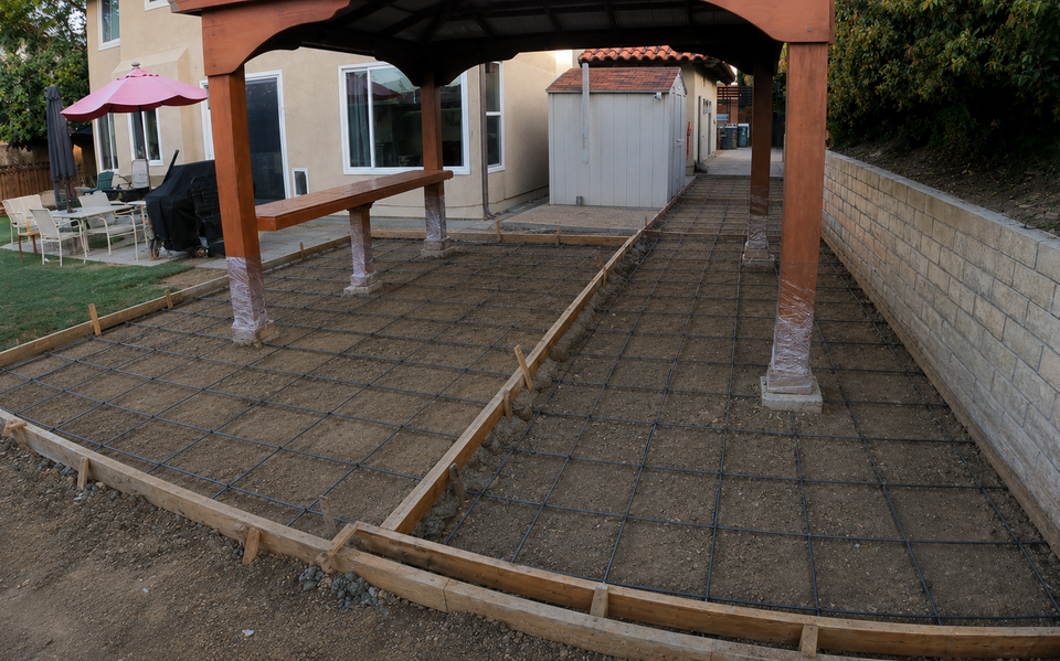Backyard concrete patio prepared with rebar reinforcement and wood form boards before concrete pouring.