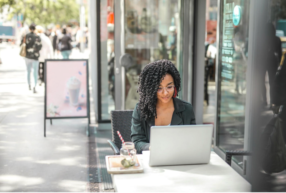 woman sitting at outdoor cafe working on laptop computer