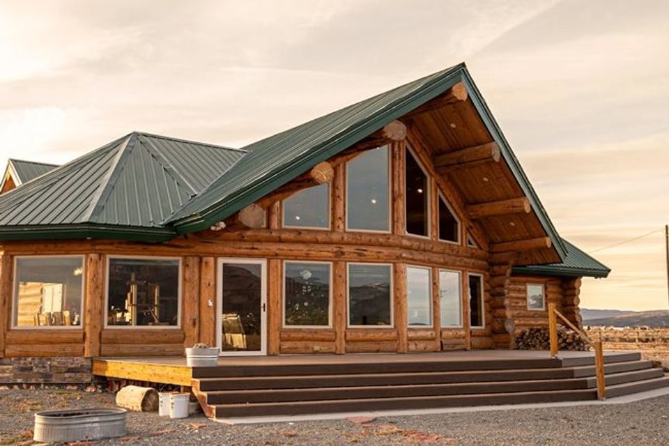 Log home with green metal roof and full height windows at sunset
