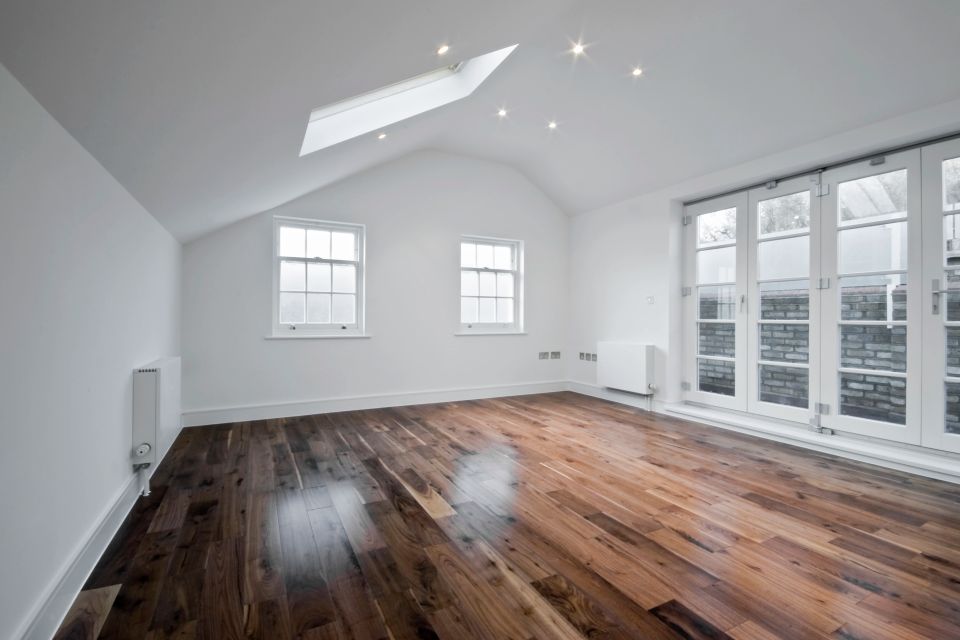 Empty attic room with newly installed hardwood flooring and skylight above white walls
