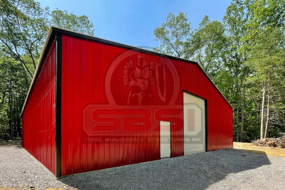 Red and black steel garage with roll up door and entry door on gravel lot with SBSI watermark representing steel garages in Alabama