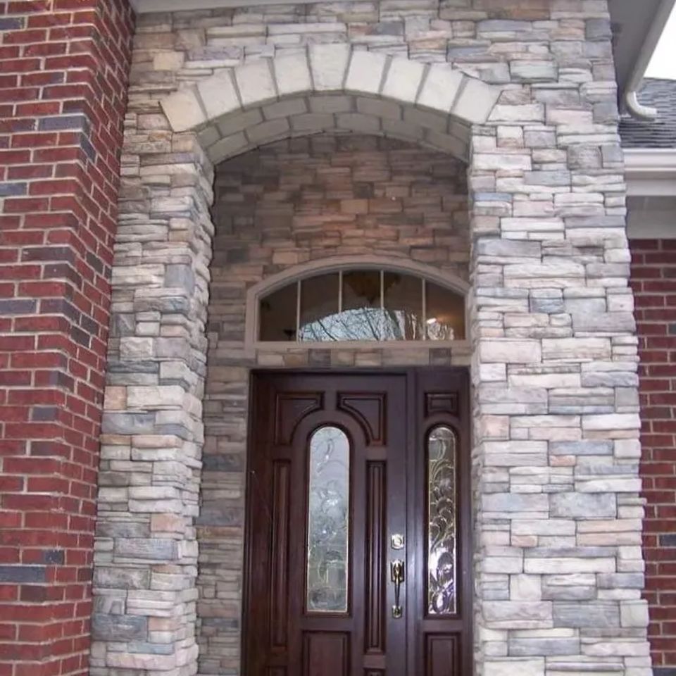 Front entry featuring light-colored veneer stone surrounding a dark wood door and arched doorway.