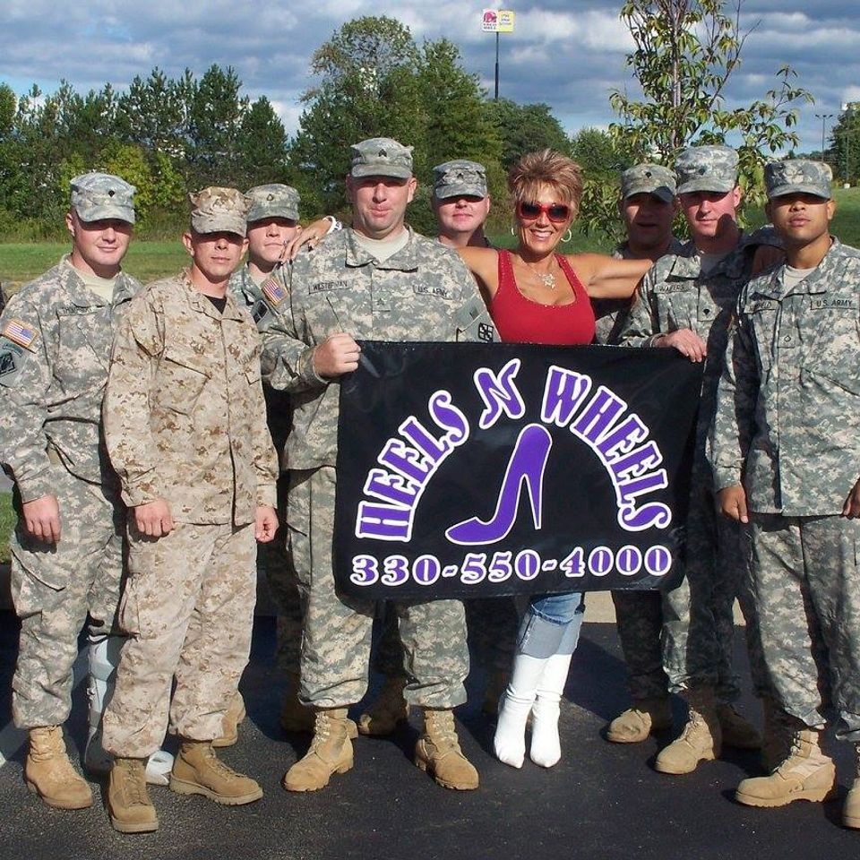 Heels N Wheels member standing with a group of U.S. Army soldiers holding a club banner.