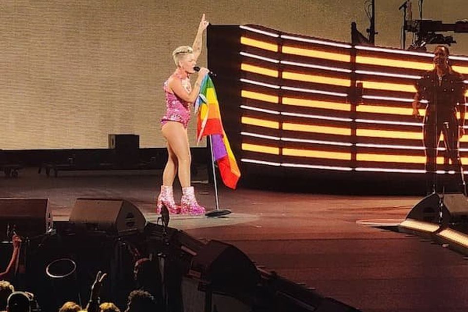 PINK in her sparkly get up singing holding a microphone with a rainbow flag on it 