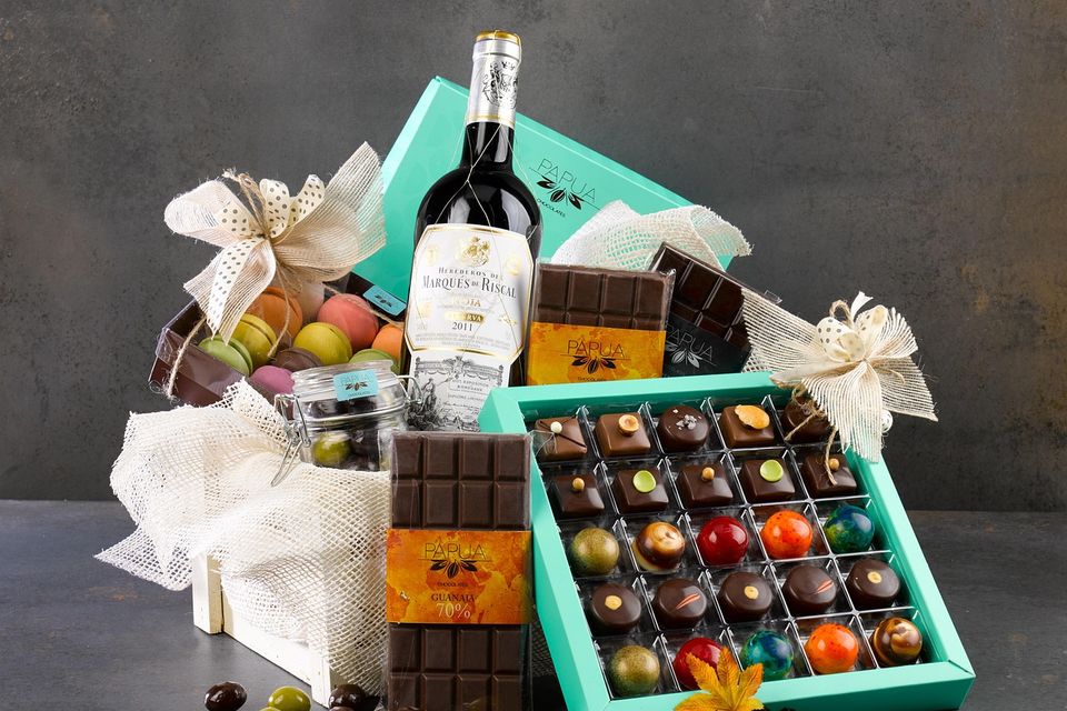 Gift crate with turquoise chocolate box, wine bottle, chocolate bars, jars of macarons and treats, decorated with burlap bows and autumn leaves.” Chocolate  and wine gift basket