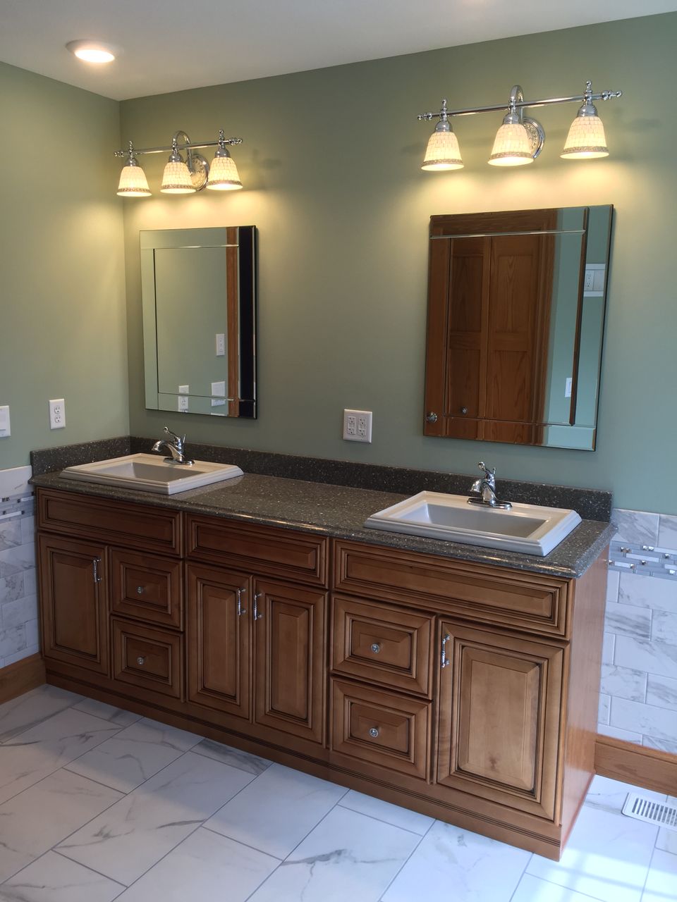 Custom bathroom featuring a double-sink vanity, wood cabinetry, granite countertop, framed mirrors, and modern fixtures.