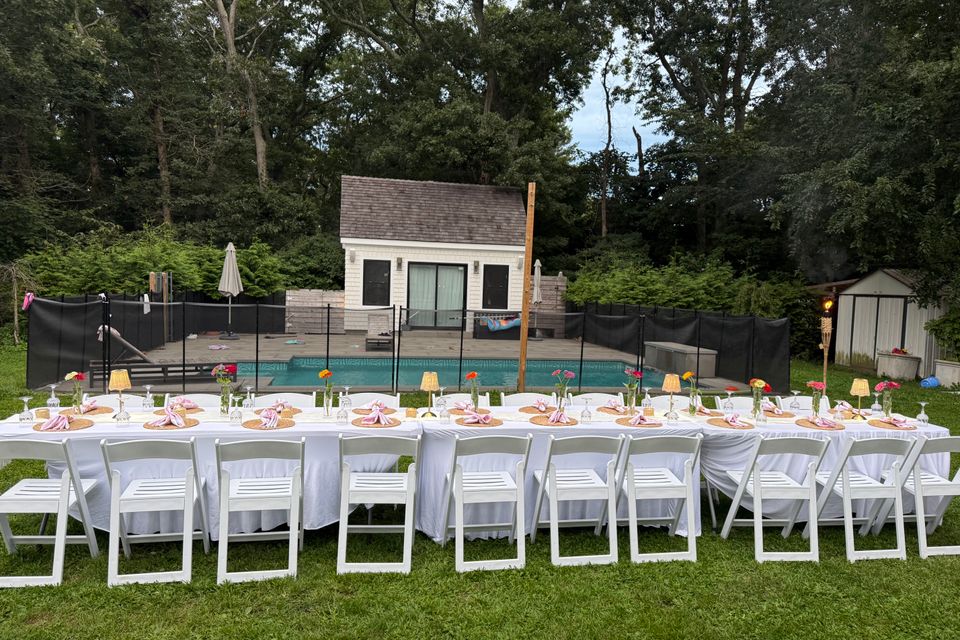 Long poolside banquet tables with pink napkins and zinnia bud vases in a Hamptons NY backyard