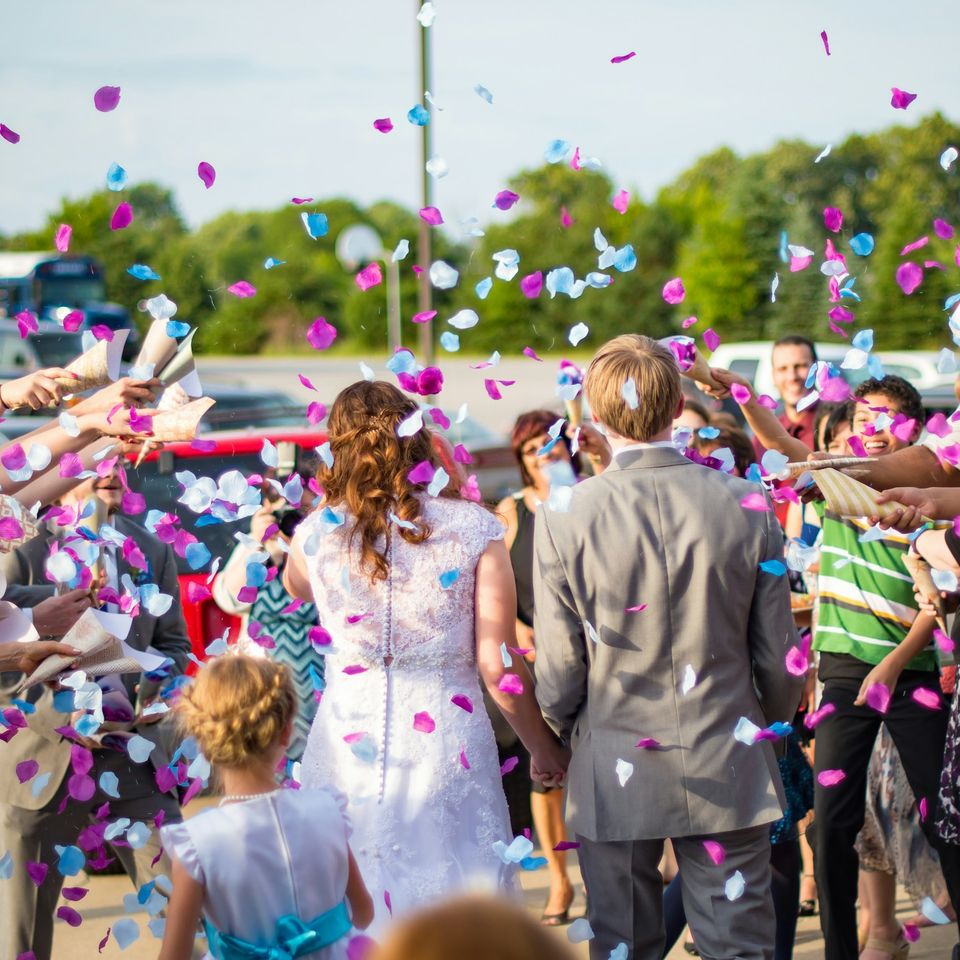 Couple walking while guests cheer and throw confetti. 