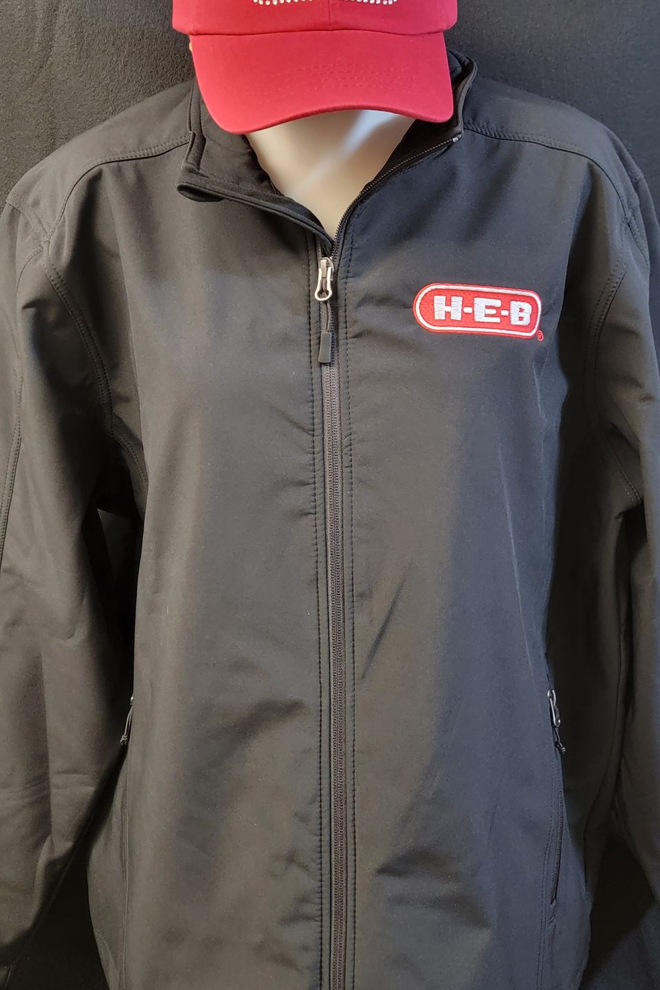 Embroidery Example - HEB logo on gray windbreaker, rhinestone bling HEB logo on red cap. 