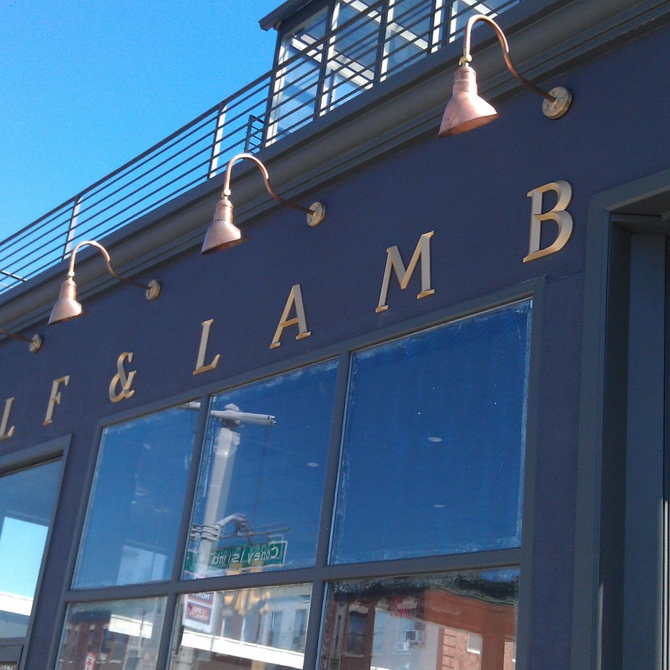 Gold pin-mounted serif letters spanning a dark navy storefront facade beneath copper gooseneck lights