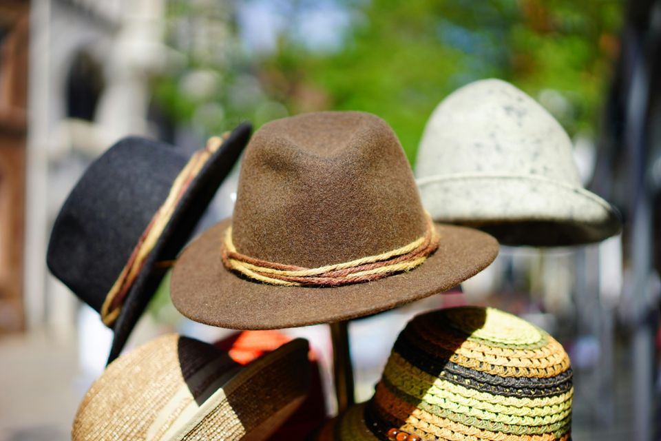 black, brown, white, and twead hats in a stand in the outdoors. 