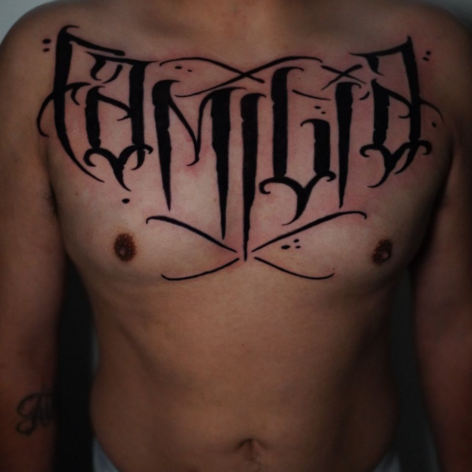 Image of a man with a large tattoo saying "Familia" across his broad chest. Tatto is black ink only