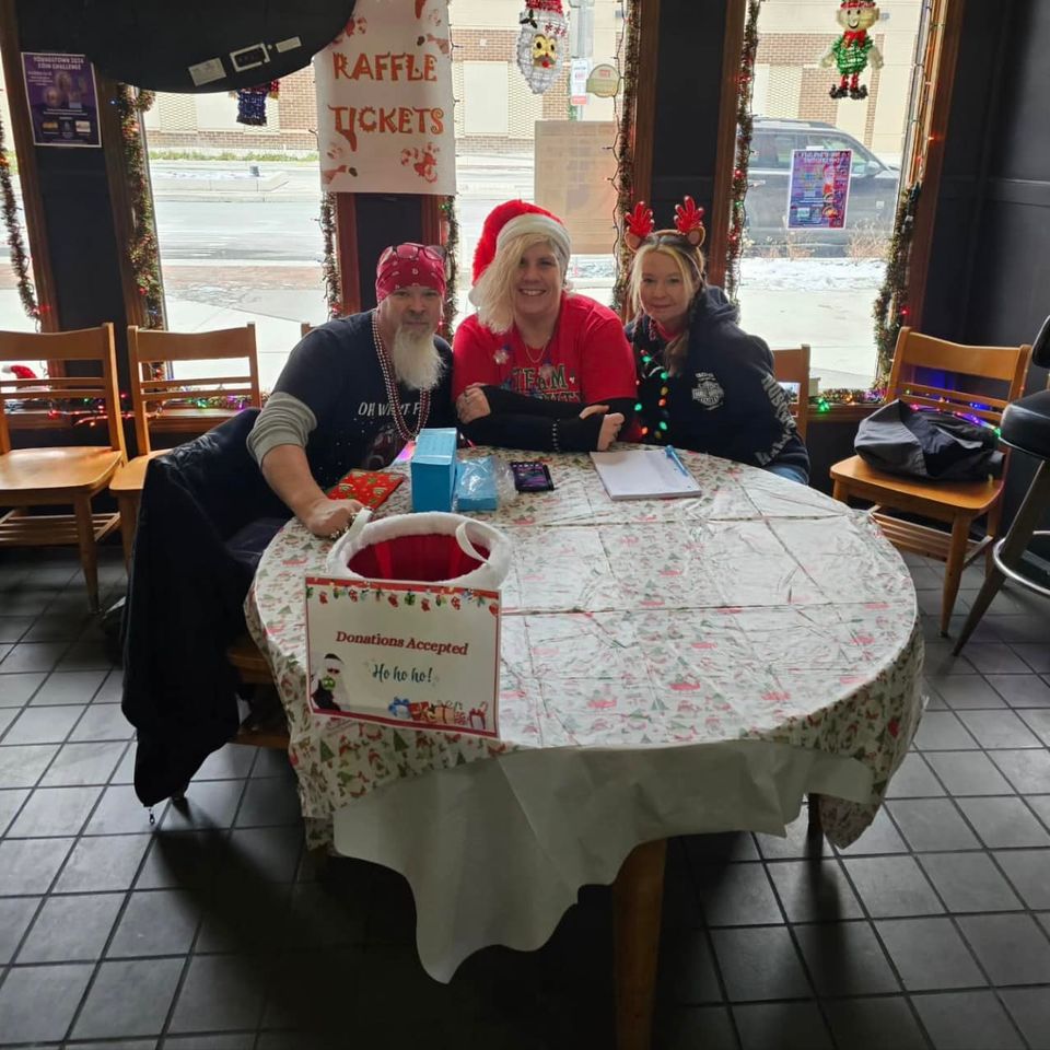 Three volunteers seated at a decorated table during a Christmas-themed fundraising event.