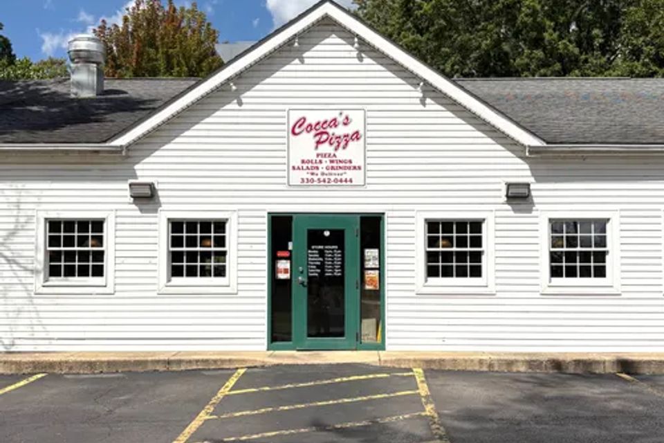 Cocca’s Pizza New Middletown, Ohio storefront featuring a white-sided building, green entrance doors, and a centered Cocca’s Pizza sign above the entrance.