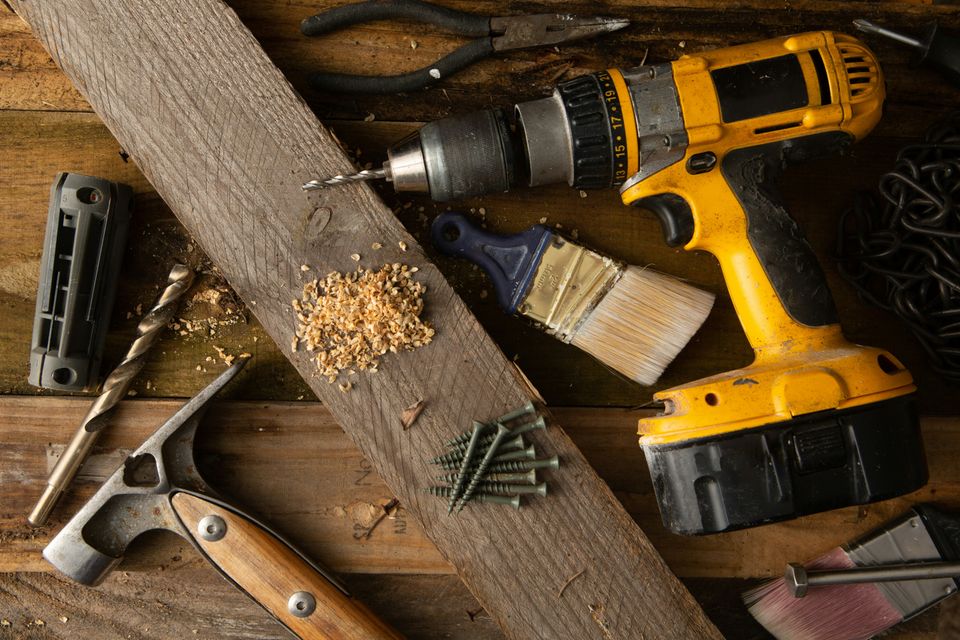 Service business tools including a power drill, hammer, screws, and brushes on a wooden workbench