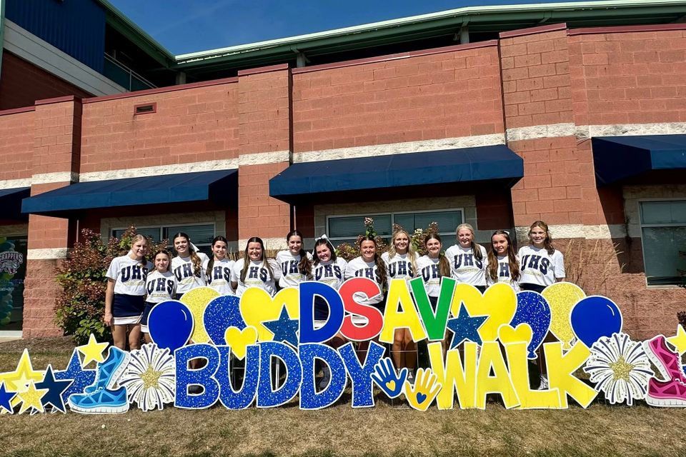 High school cheerleaders posing behind a colorful DSAV Buddy Walk display outside the Buddy Walk event venue.