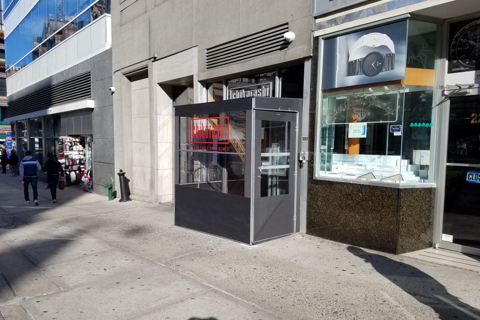 Compact dark grey vestibule with a clear glass door enclosing a single storefront entrance on a New York City sidewalk