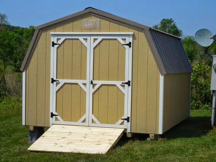 Tan mini barn shed with white trim doors and wood ramp installed in East Tennessee