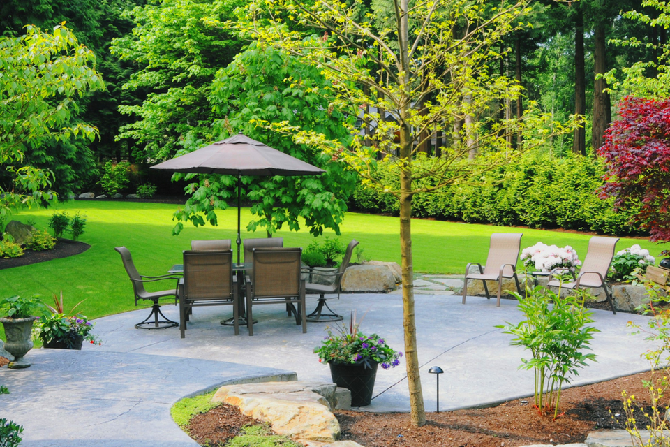 Custom backyard patio with decorative concrete, seating area, landscaped garden beds, mature trees, and professionally designed outdoor living space by R.E.P. Companies.