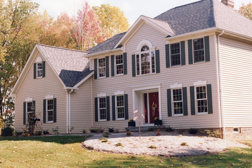 Two-story custom home featuring a traditional exterior with vinyl siding, black shutters, a covered entryway, and professionally landscaped front yard.