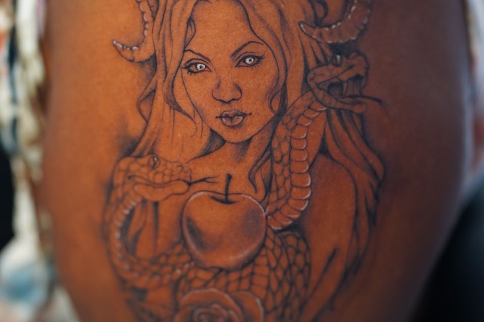 Image of a large shoulder tattoo of a woman with horns and a serpent and an apple with white highlights
