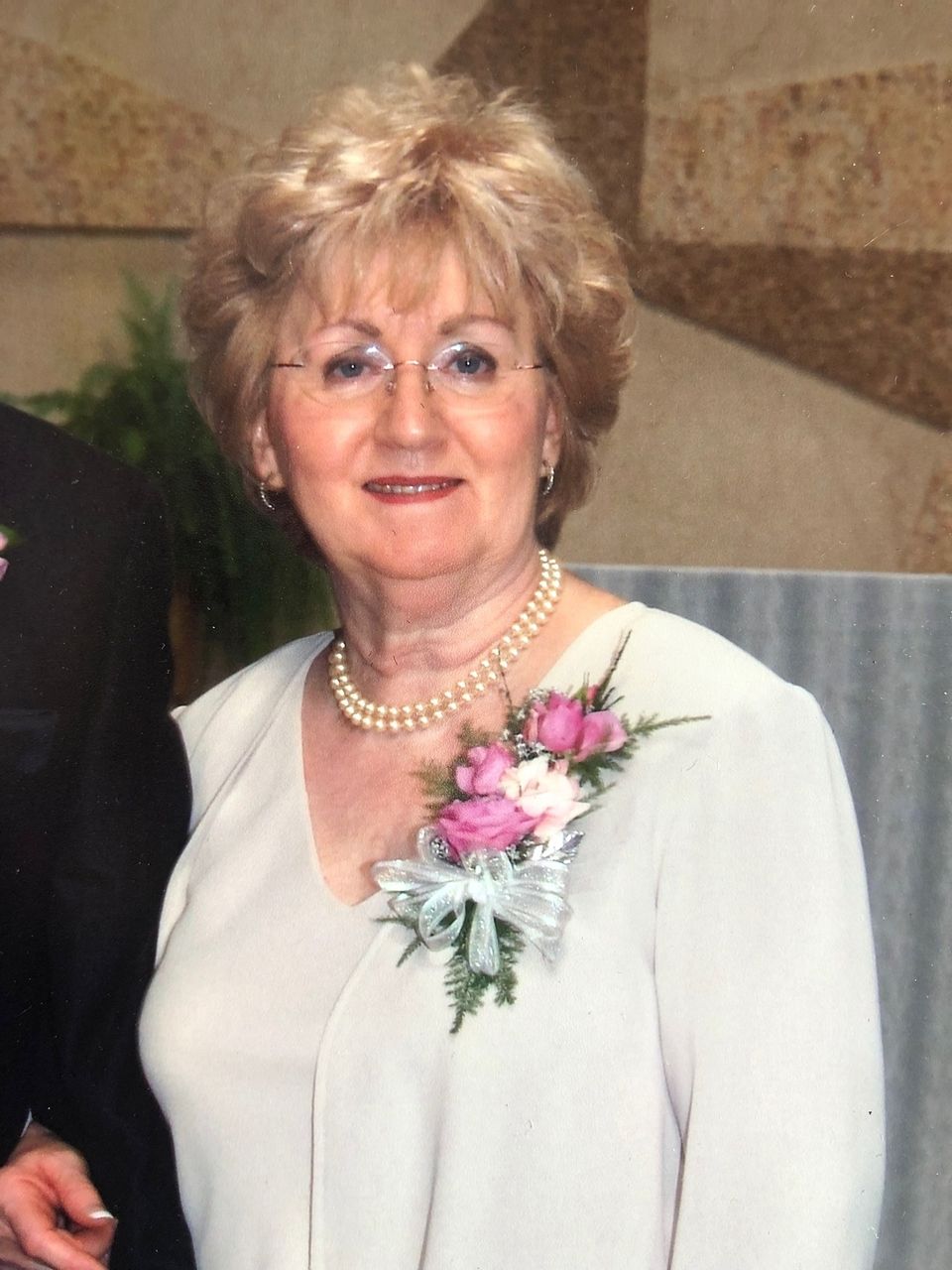 Portrait of Marilyn Jacobs, owner of Shears Wigs & Hairpieces Salon, smiling while wearing a light-colored dress, pearl necklace, and floral corsage.