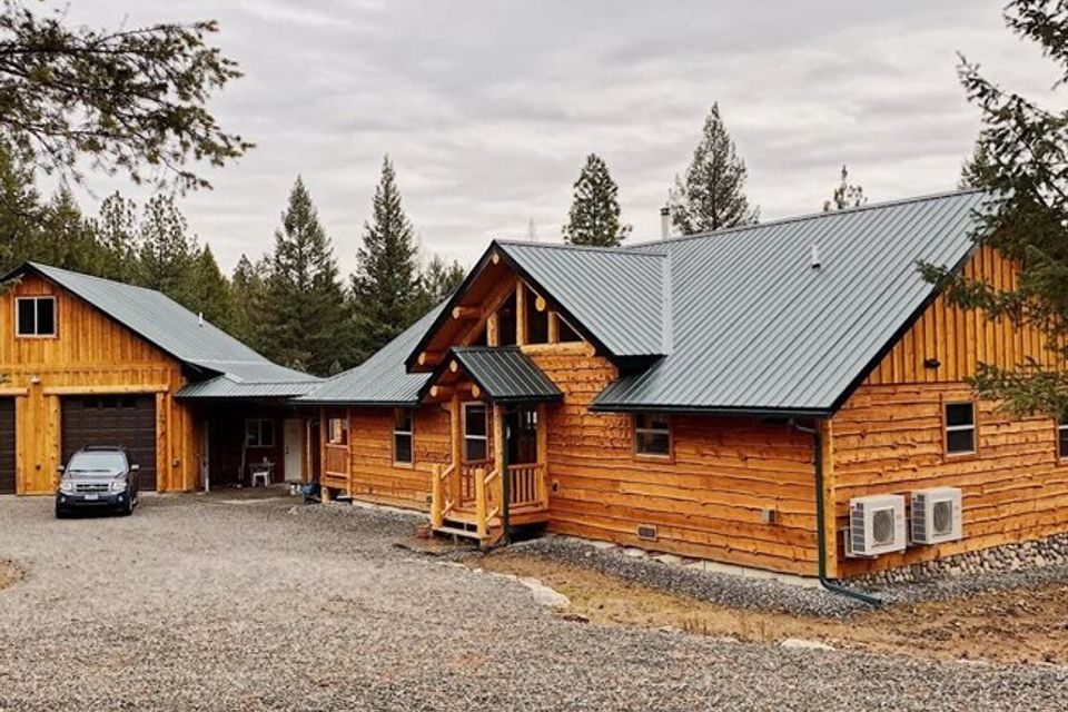 Log home with attached garage, green metal roof, and covered entry