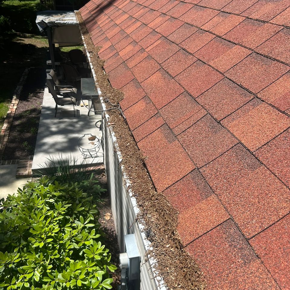 Clogged gutter filled with debris alongside red shingle roof before gutter cleaning in Harrisburg PA