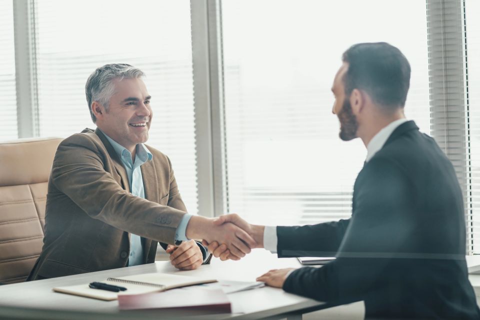 The two happy businessmen handshaking over the glass in the office
