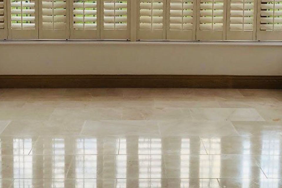 Empty room with glossy beige marble floor, white plantation shutters, and natural light reflections