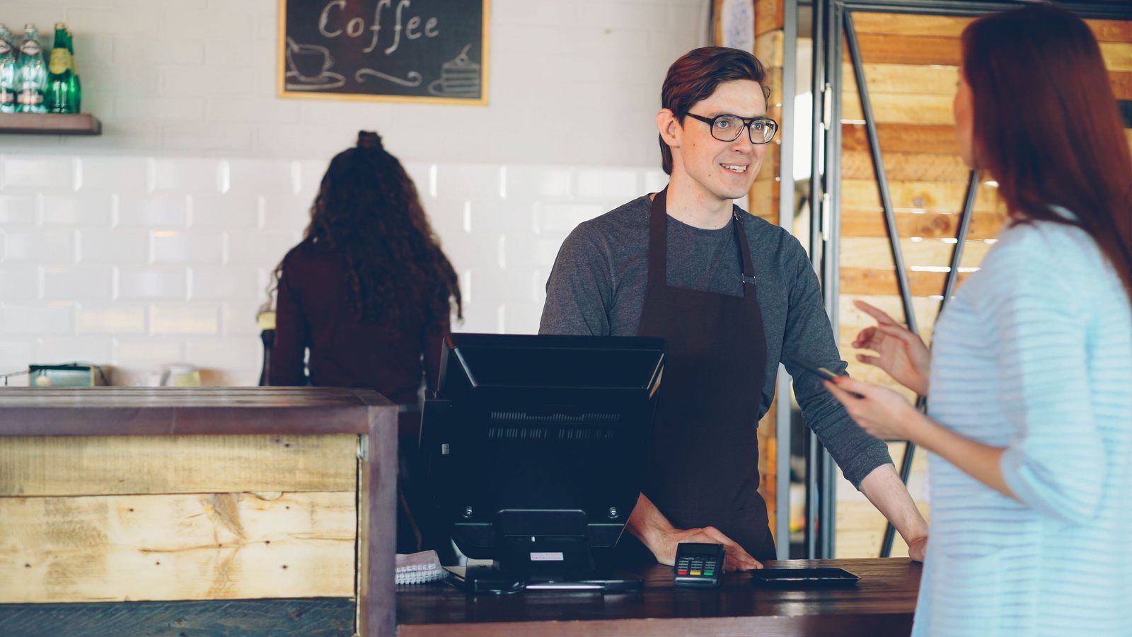 Barista helping a customer at a coffee shop counter with a point-of-sale terminal