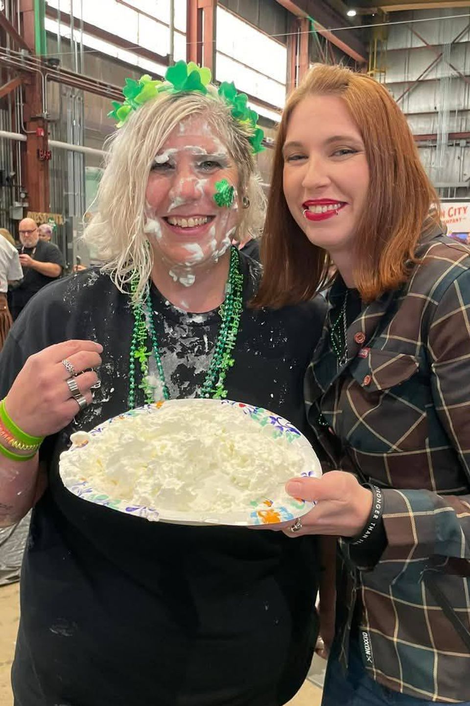 Two women smiling together while holding a pie plate during a community event.