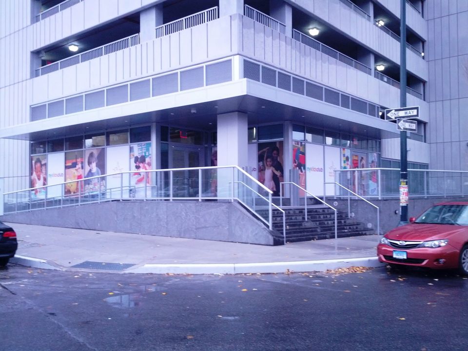 Printed window graphics with photos of children and NY Kids Club logos wrapping the ground floor windows of a corner building in Long Island City