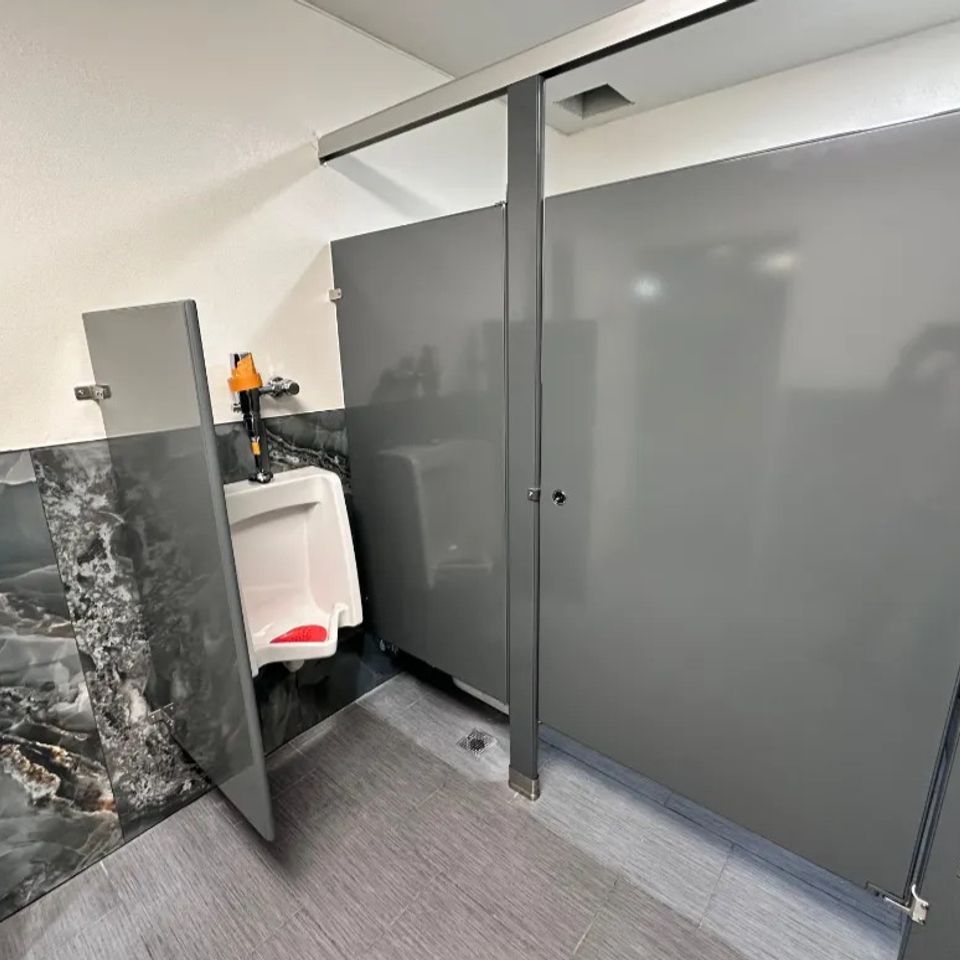 A urinal next to newly installed bathroom partitions done by Pabst Leyton