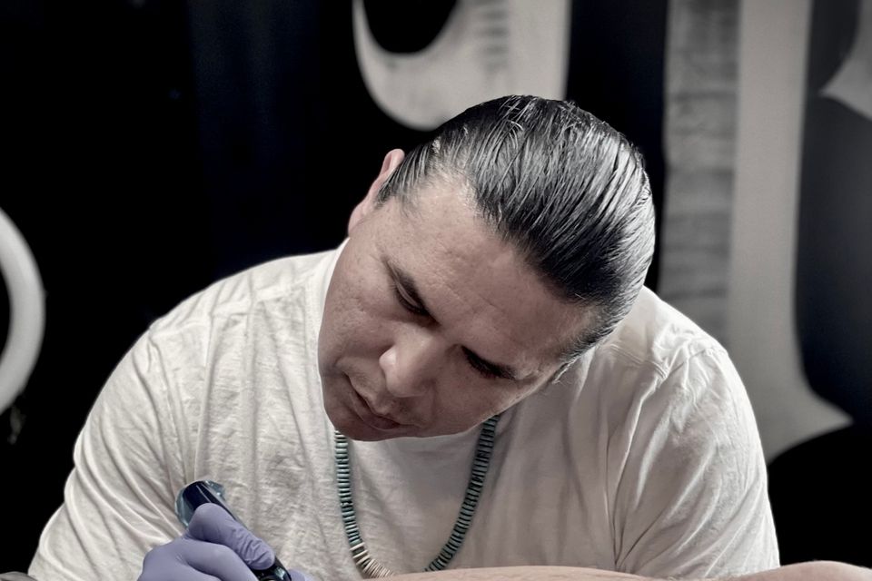 Image of a focused Adrian Anderson laying down some ink on a customer's lower calf, tattoo is not seen just a frontal view of Adrian at work