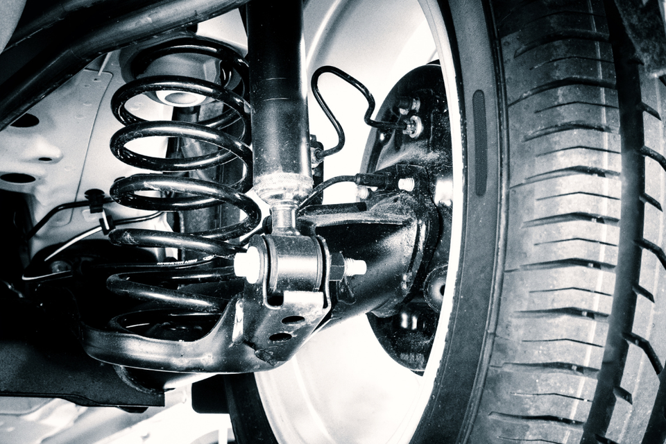 Close-up of a vehicle's shock absorber, coil spring, and suspension components during inspection or repair.