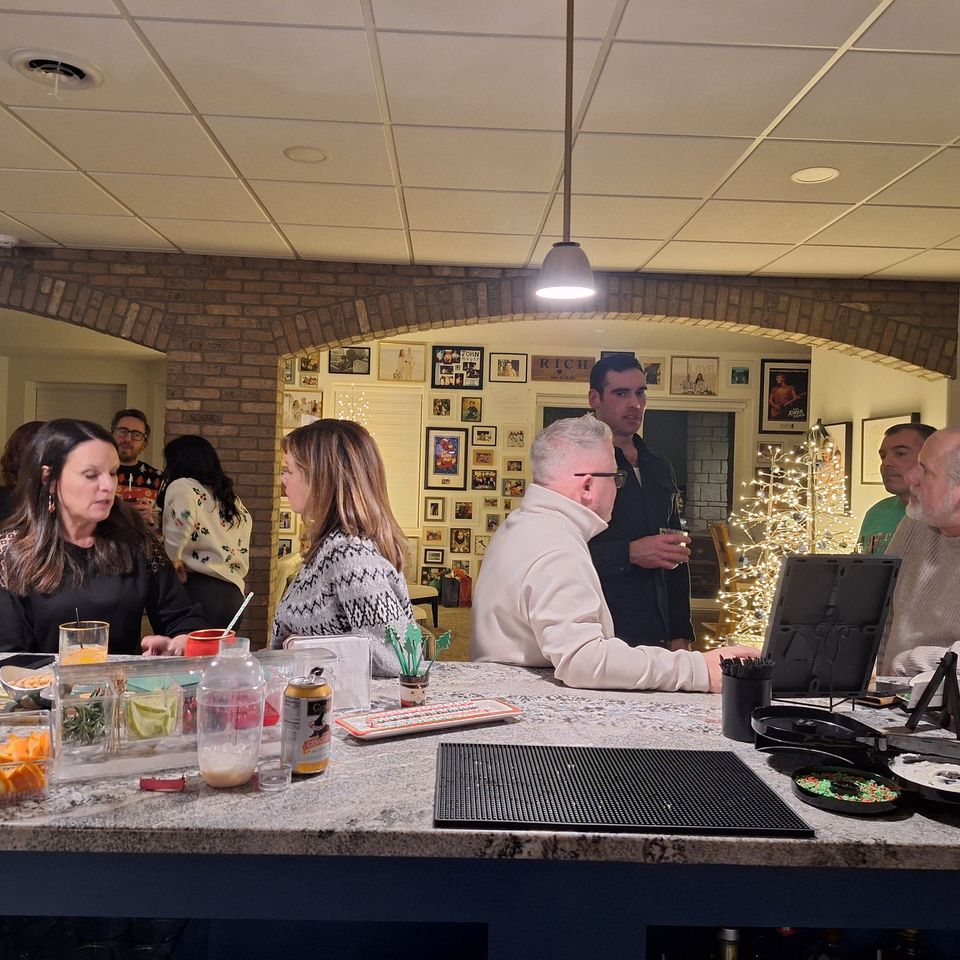 People gathered around a bar area with drinks and garnishes at a holiday party