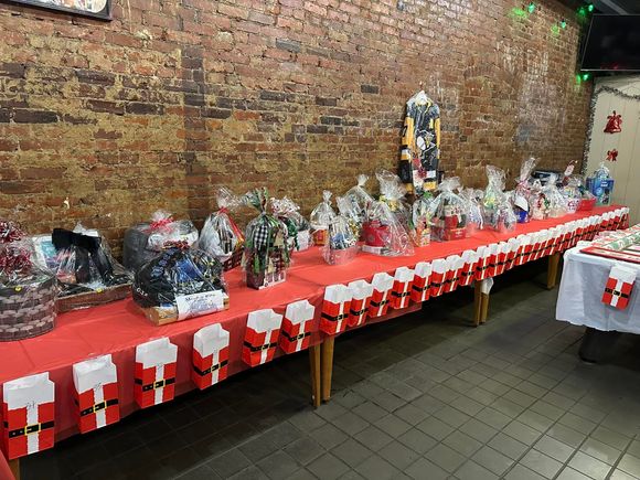 Long table displaying raffle baskets, prizes, and holiday-themed gift bags during a community event.