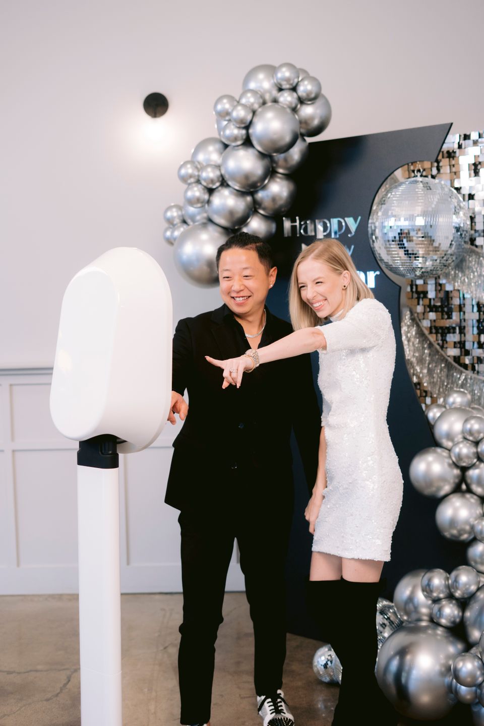 Two guests interacting with a sleek photo booth during a celebration.