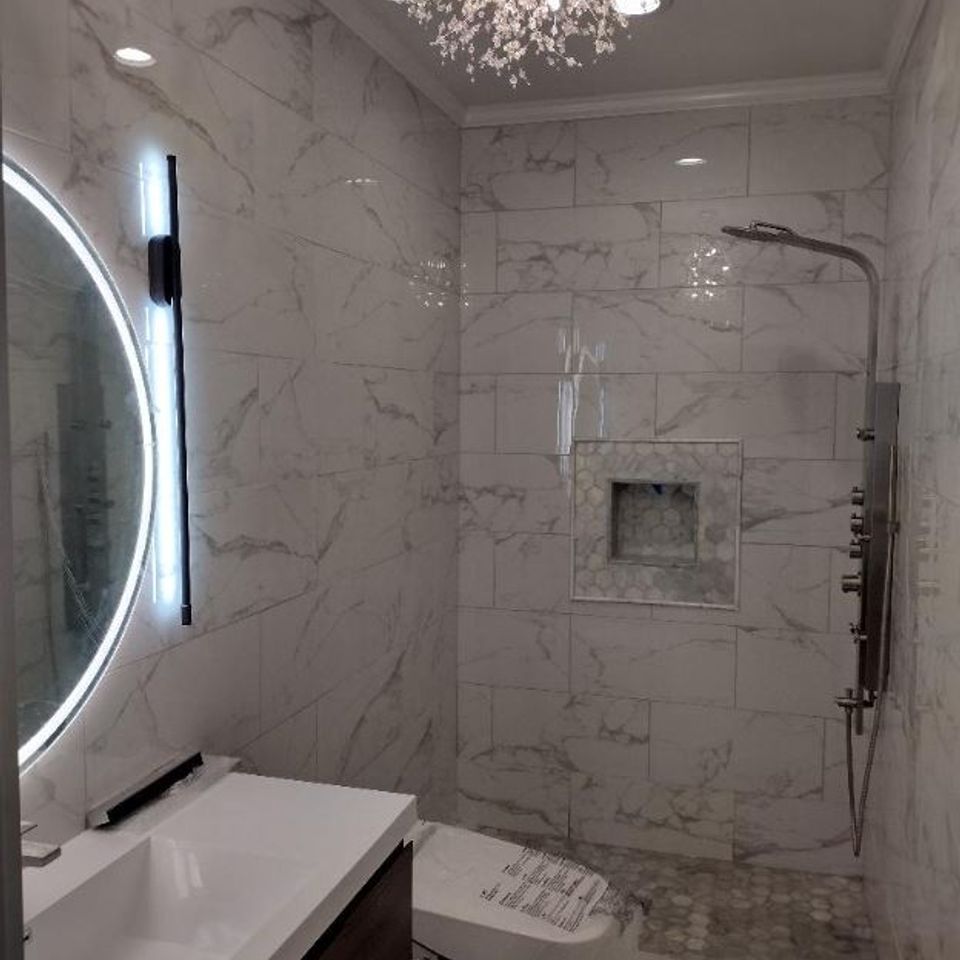 Marble tile bathroom remodel with round lit mirror and rain shower by general contractor in Suffolk County NY