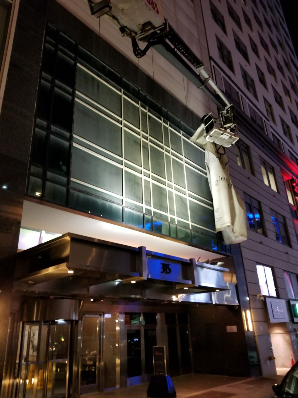 Banner being handled from an extended boom lift on a Manhattan hotel facade at night