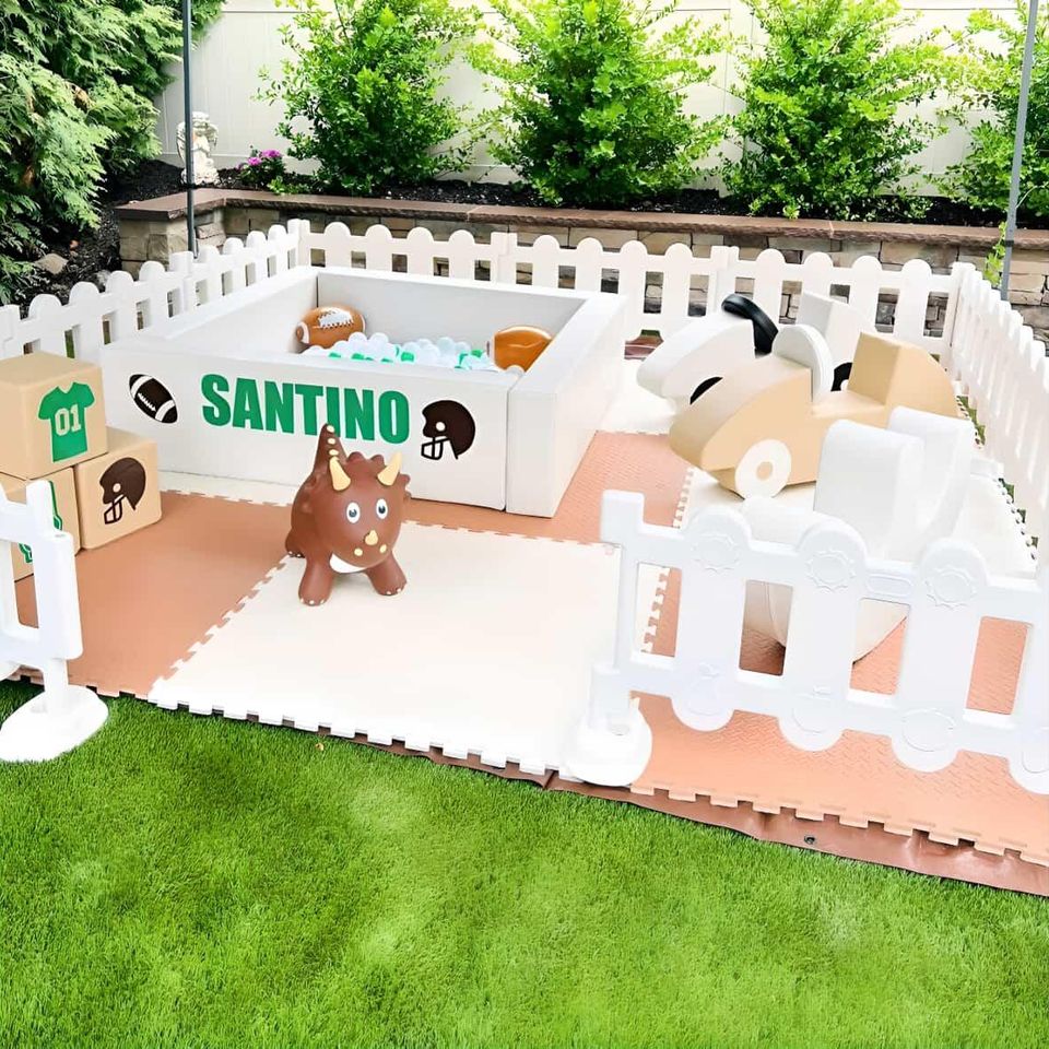 Custom soft play area rental with white picket fence, ball pit, ride-on toys, and personalized Santino theme by Aldys Events