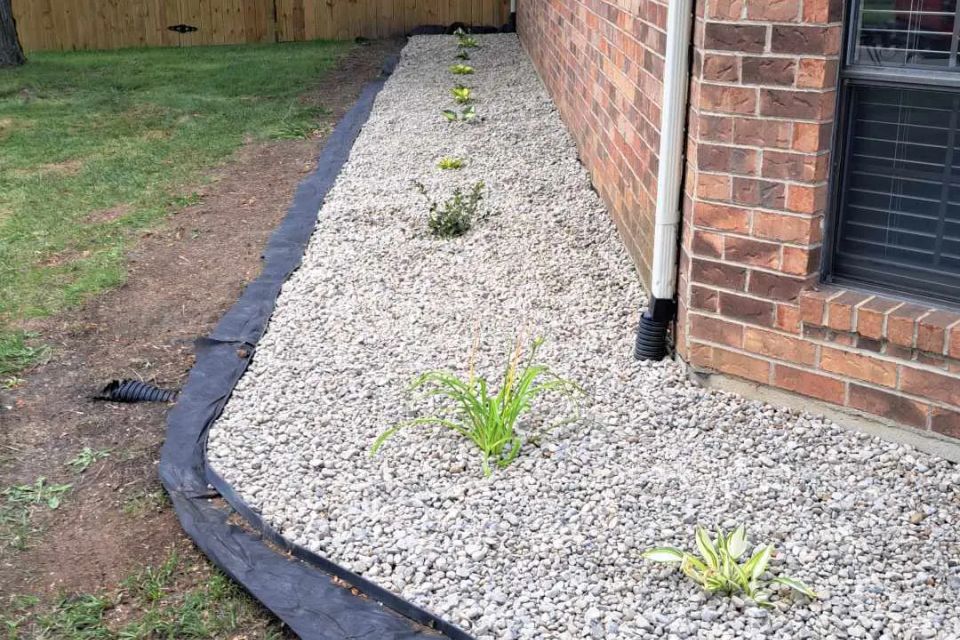 Side view of a home with newly installed white gravel landscaping and decorative plants.